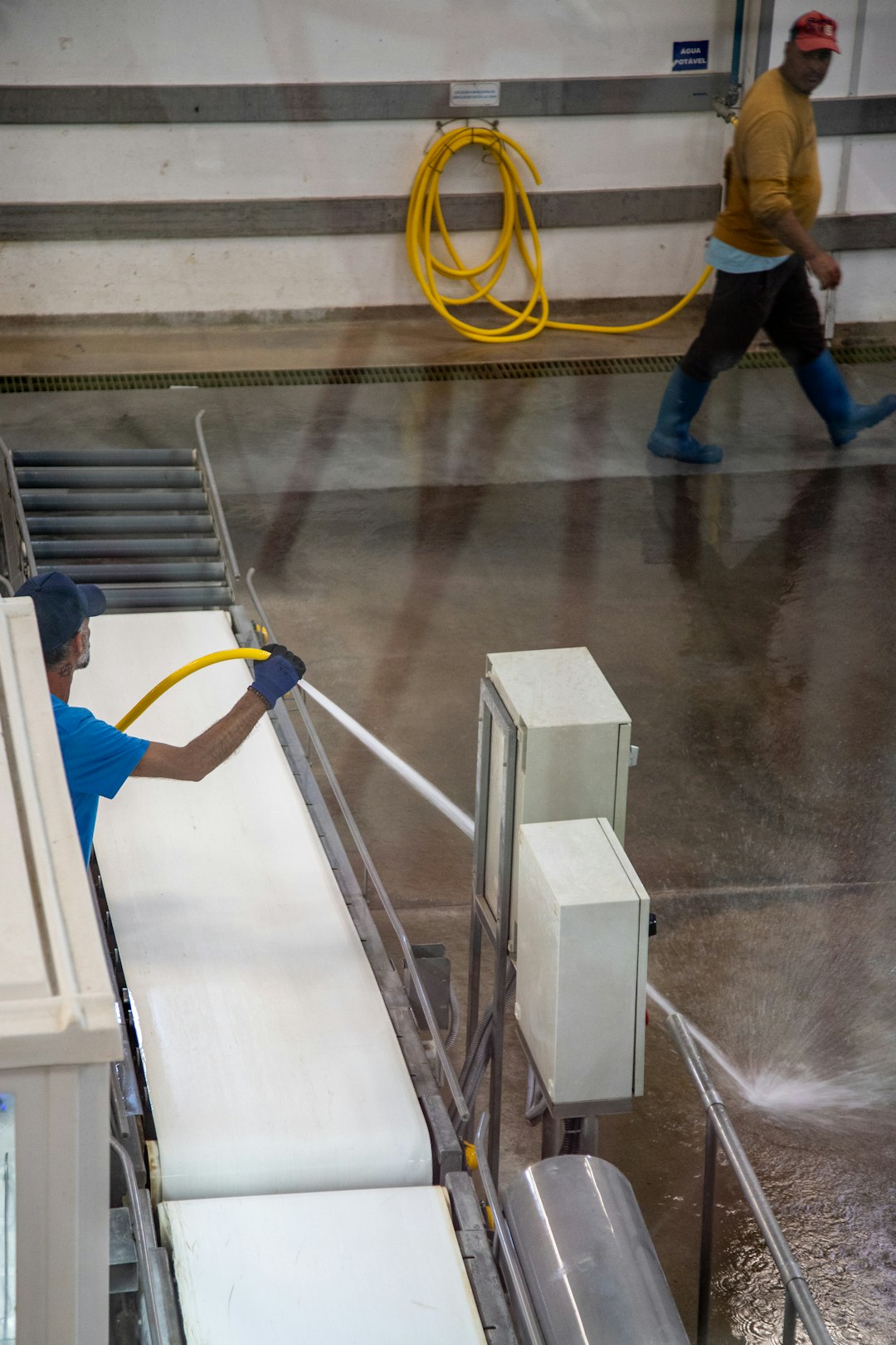 workers-cleaning-a-conveyor-belt-with-hoses-in-a-factory-zmvz6zgyaae